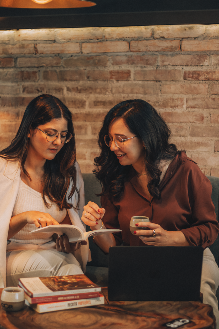 Two women discussing ideas with a book and laptop in a cozy cafe.