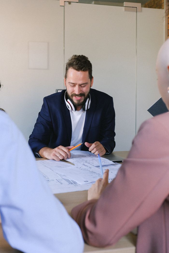 Cheerful male with crop anonymous colleagues discussing data in papers at table in conference in business office
